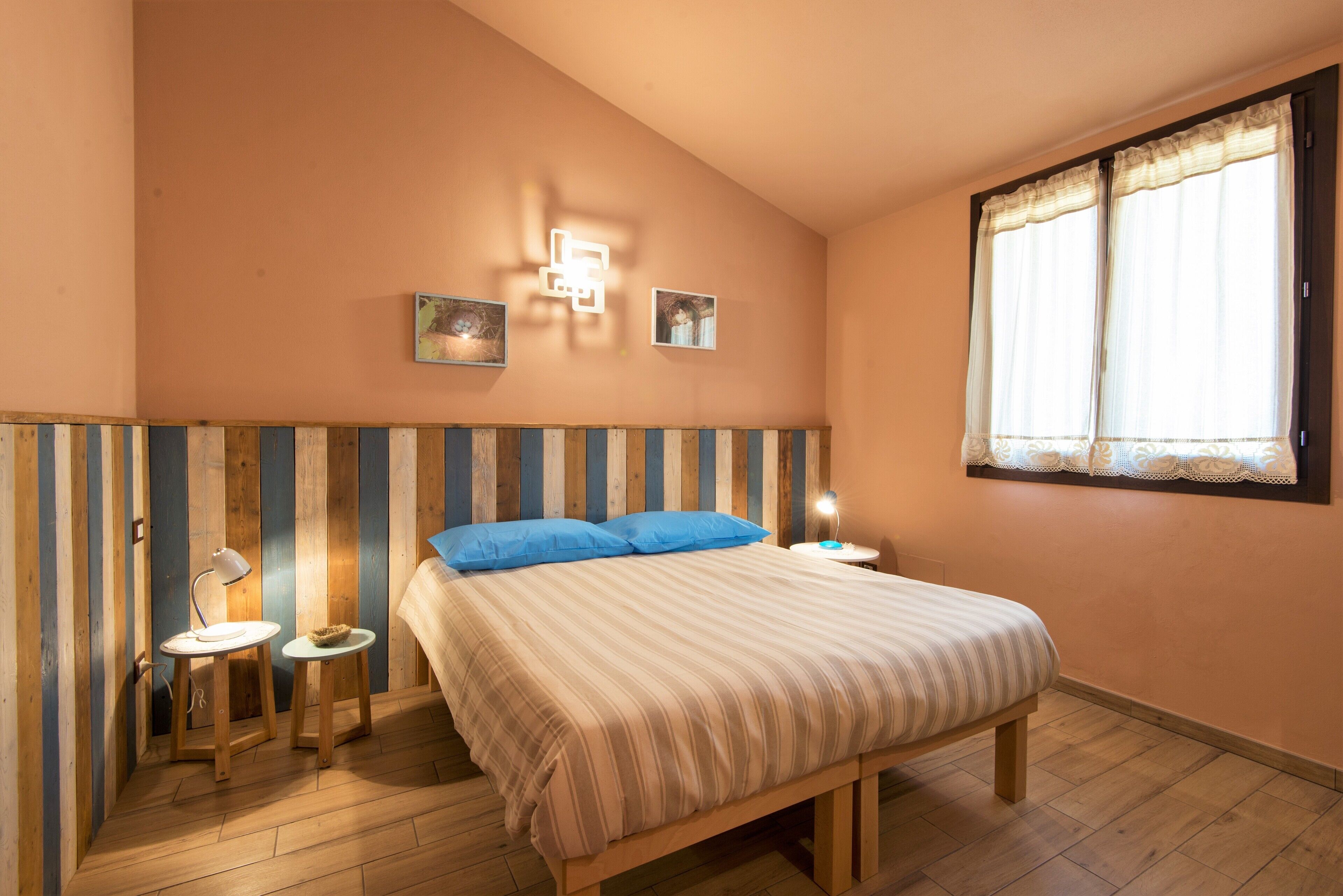 A bedroom with a bed, two bedside tables, a wall-mounted light, and a window with curtains.