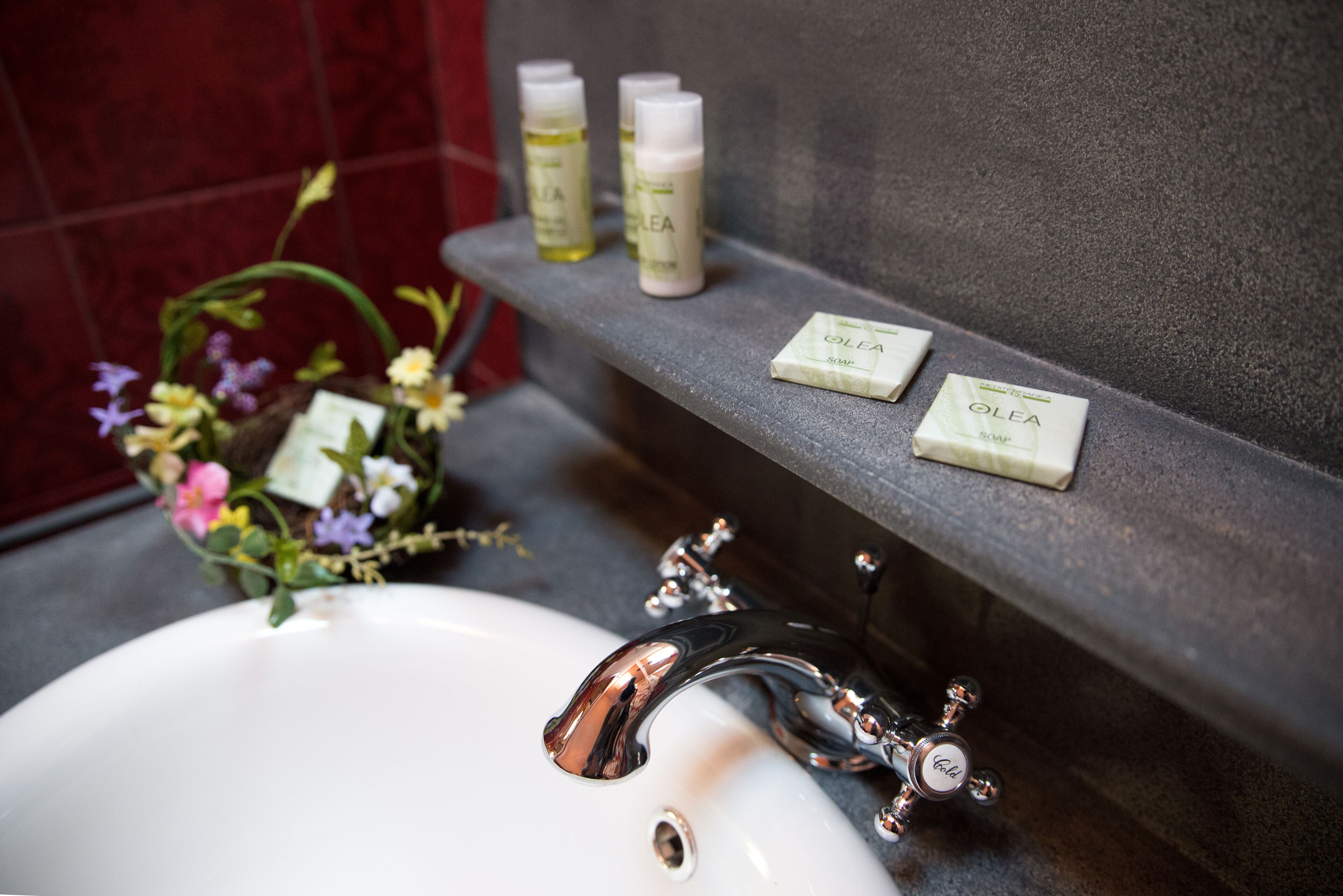 A bathroom with a white sink, chrome faucet, and a shelf holding toiletry bottles and soap.