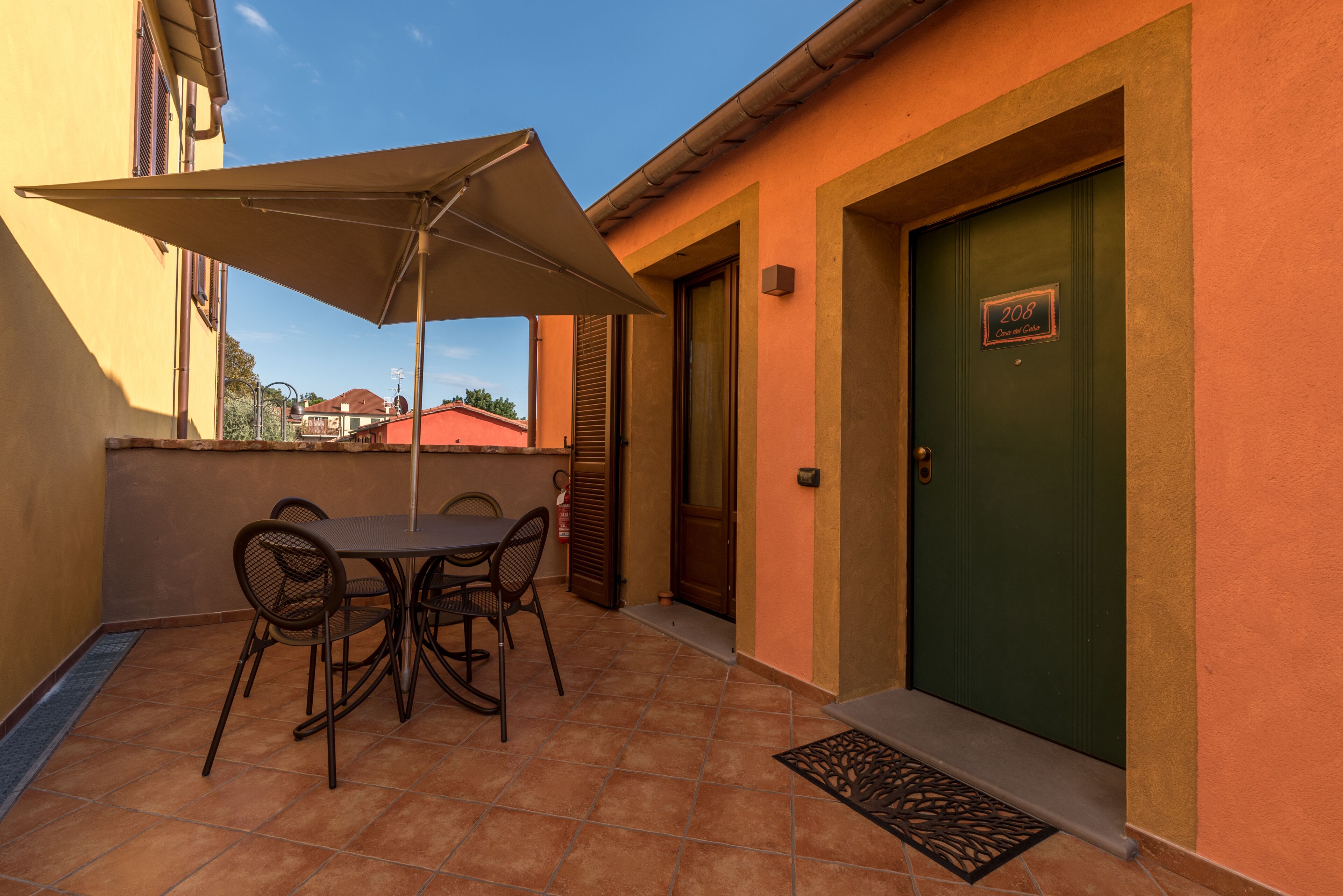 Un patio con una mesa y sillas, una puerta con una placa de número y un piso de baldosas.