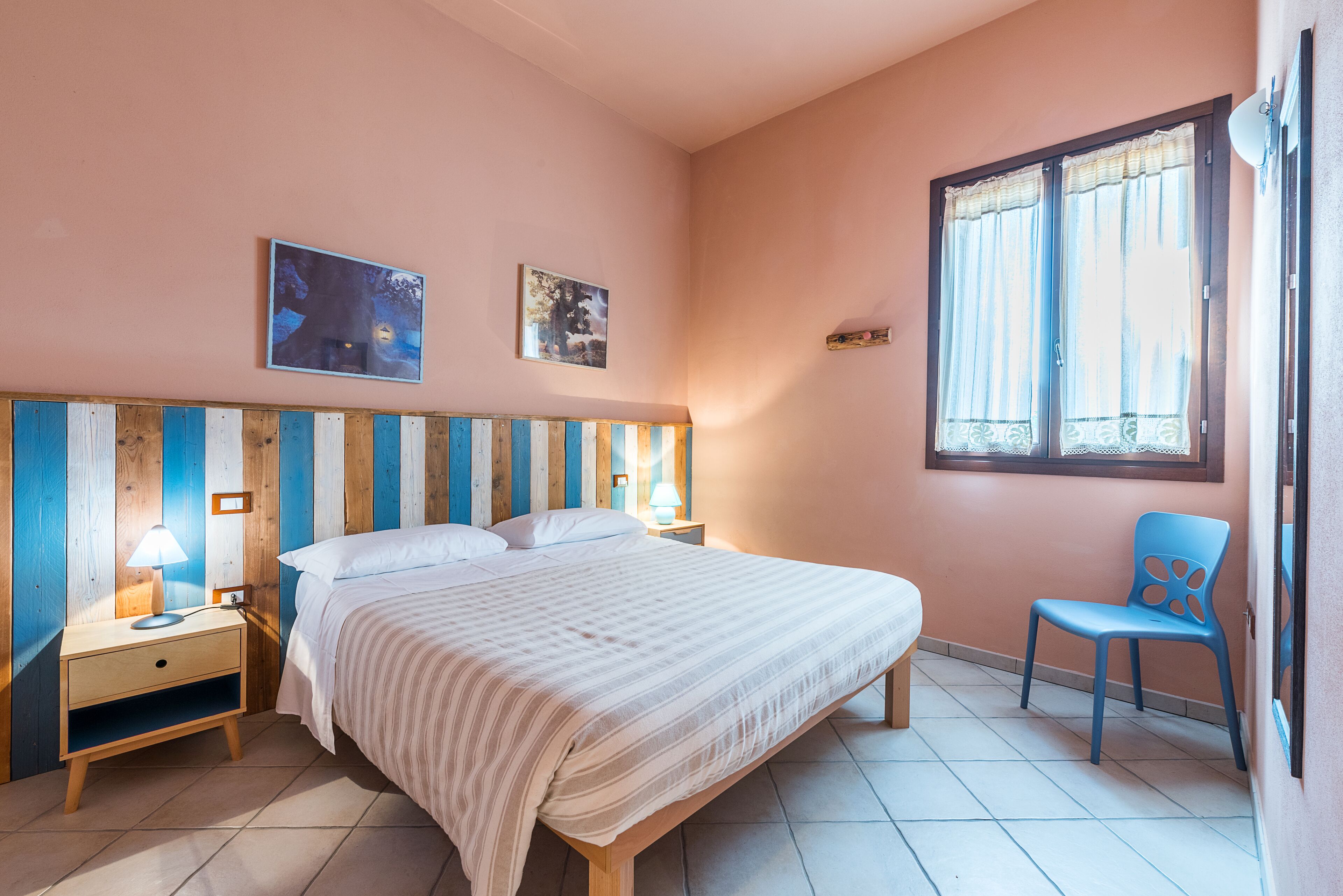 A bedroom with a bed, nightstands, a chair, and two wall-mounted pictures.