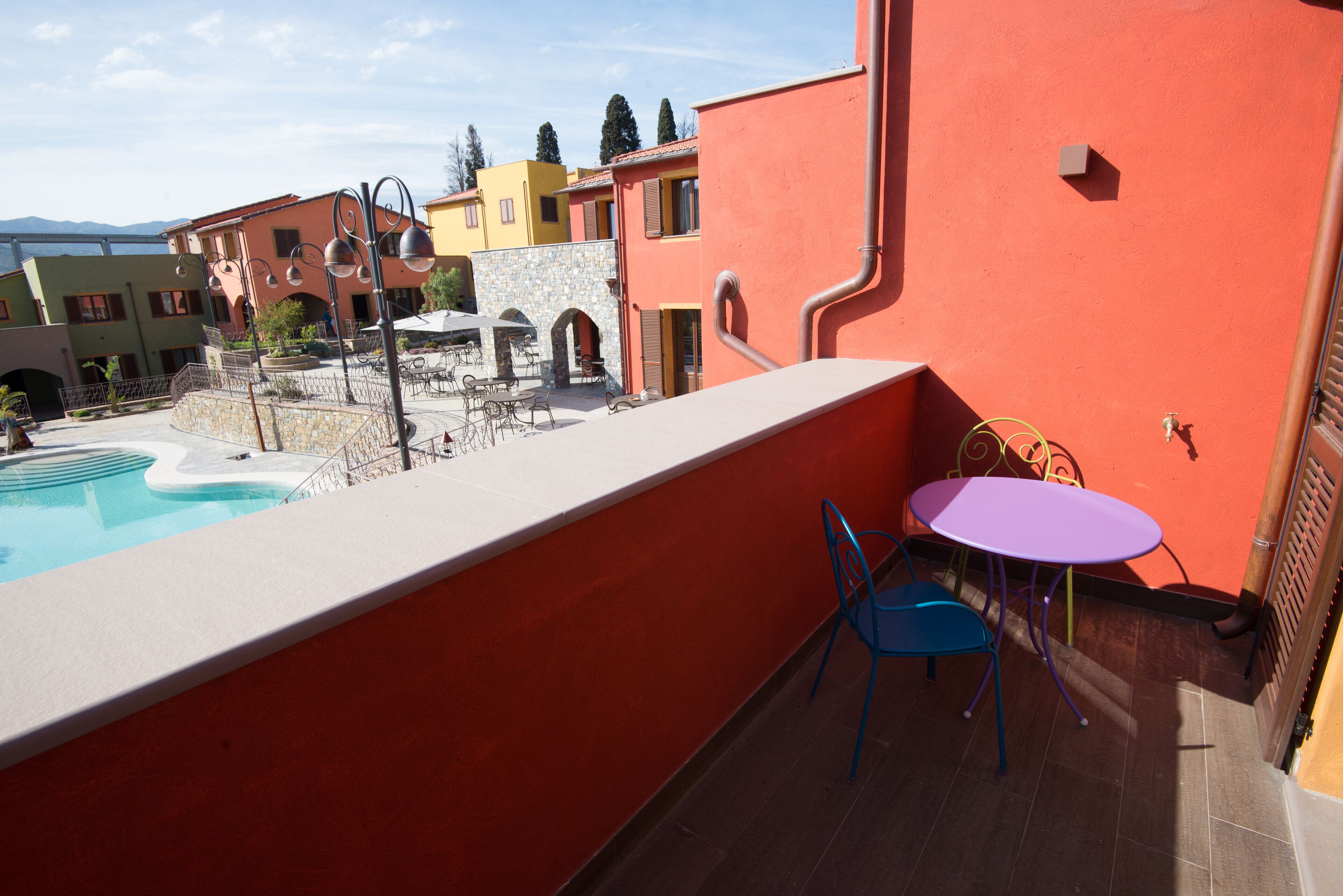 A balcony with a pool, outdoor seating, and a view of colorful buildings.