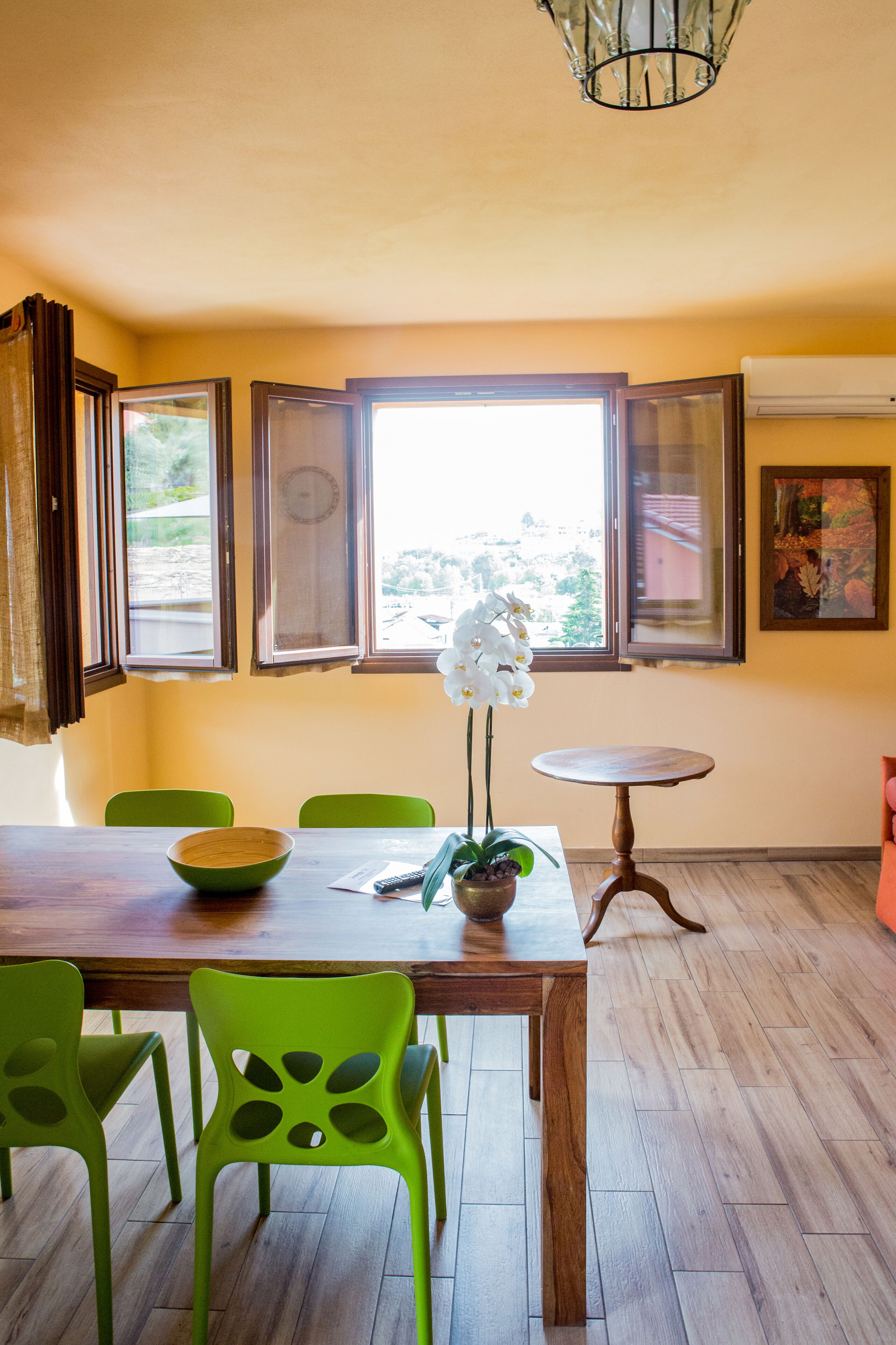 Un coin repas avec une table en bois, des chaises vertes, une orchidée en pot et une petite table ronde.