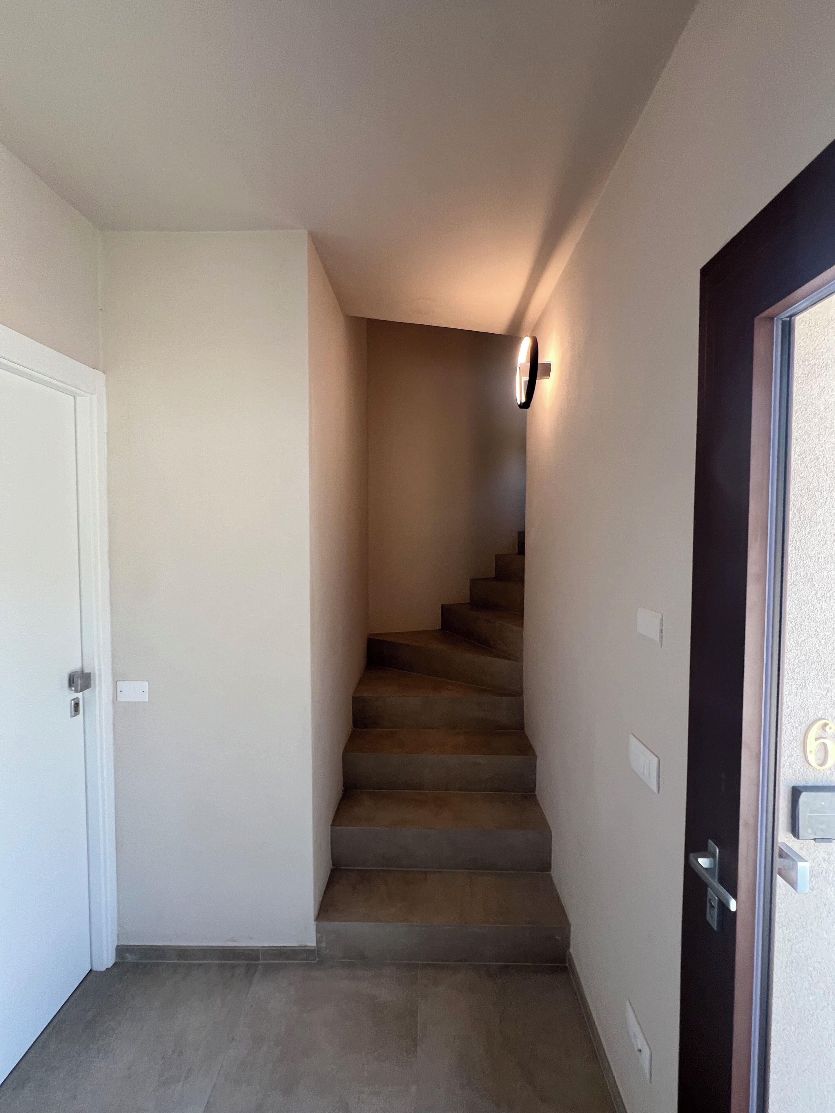 A narrow staircase with carpeted steps leading to a landing, a door on the left, and a door on the right with a number plate.