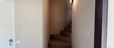 A narrow staircase with carpeted steps leading to a landing, a door on the left, and a door on the right with a number plate.