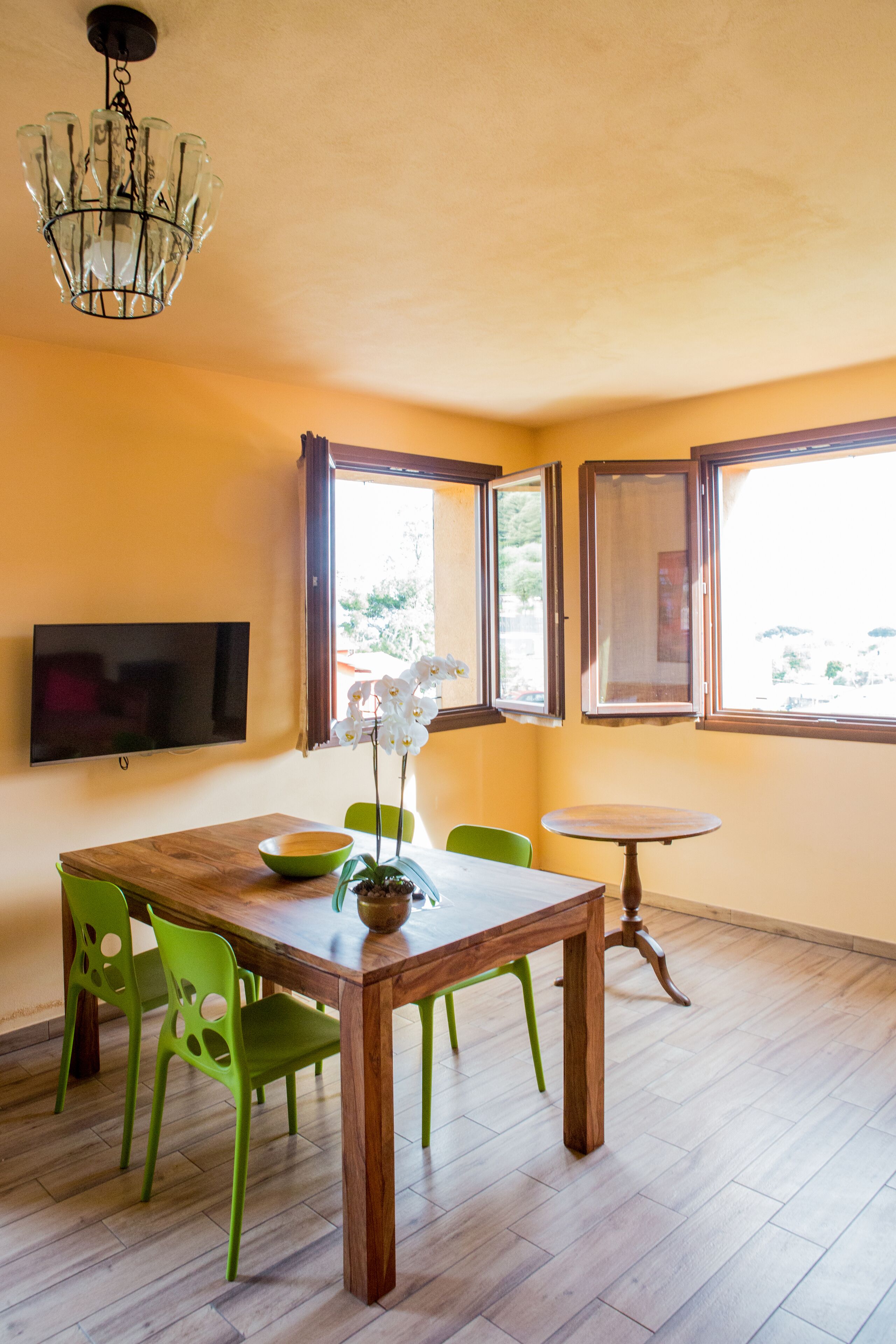 Un espace repas comprenant une table en bois, des chaises vertes, une petite table ronde et un lustre.