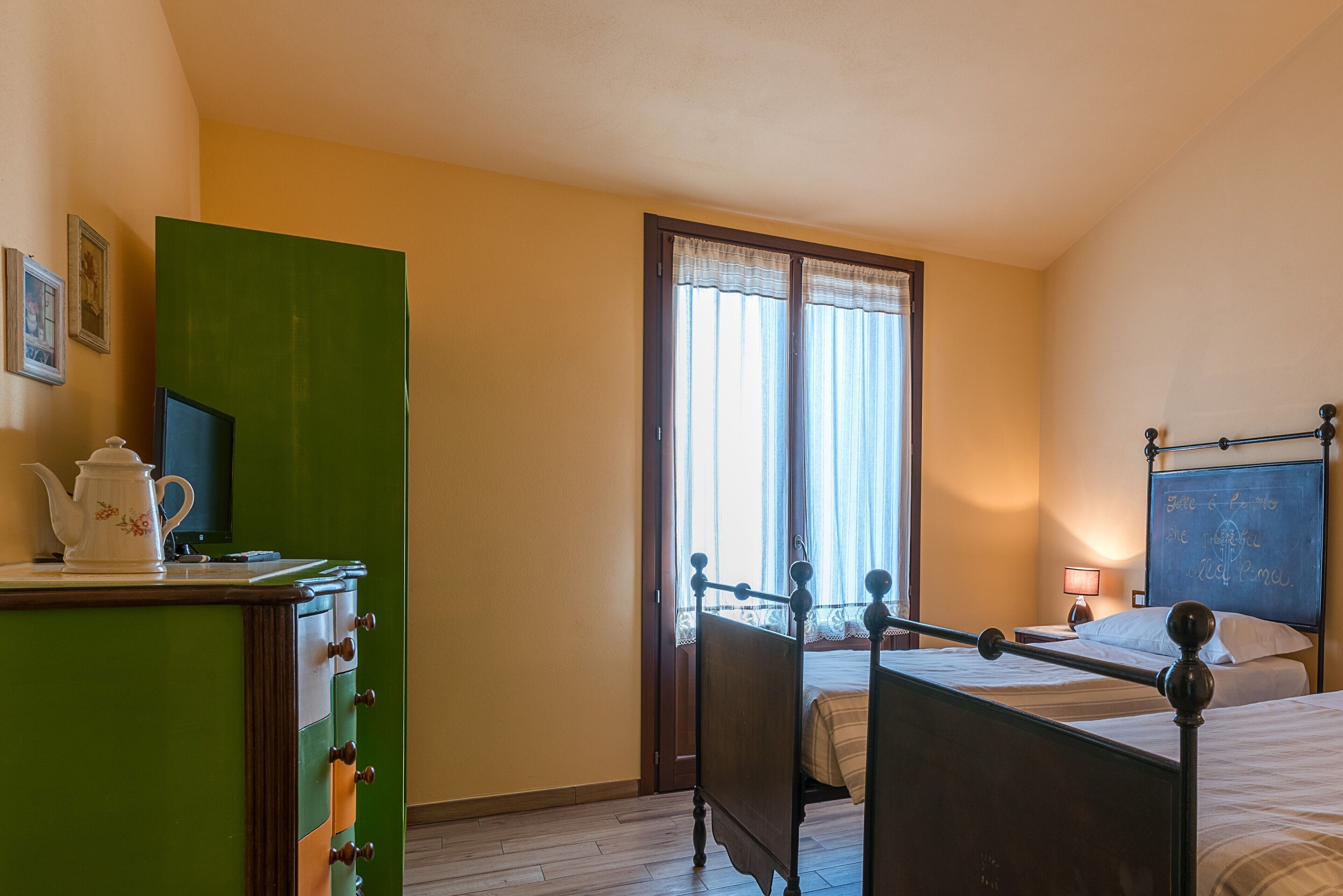 A bedroom with two beds, a green dresser, a television, and a chalkboard on the wall.