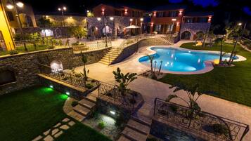A well-lit outdoor swimming pool area with stone walls, a stone staircase, and a paved walkway.