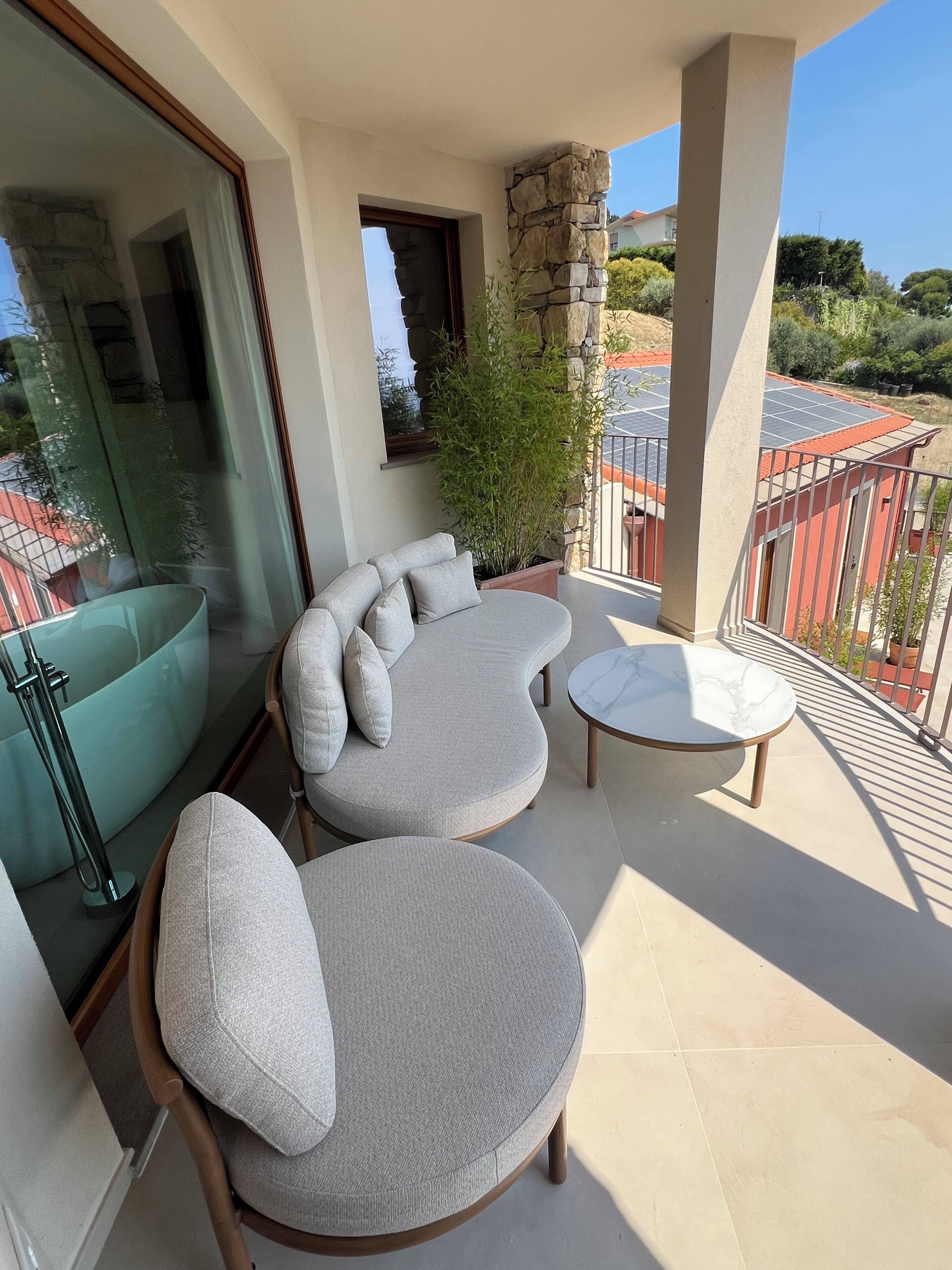 Een balkon met een gebogen bank, een ronde tafel, een potplant en uitzicht op de omgeving.