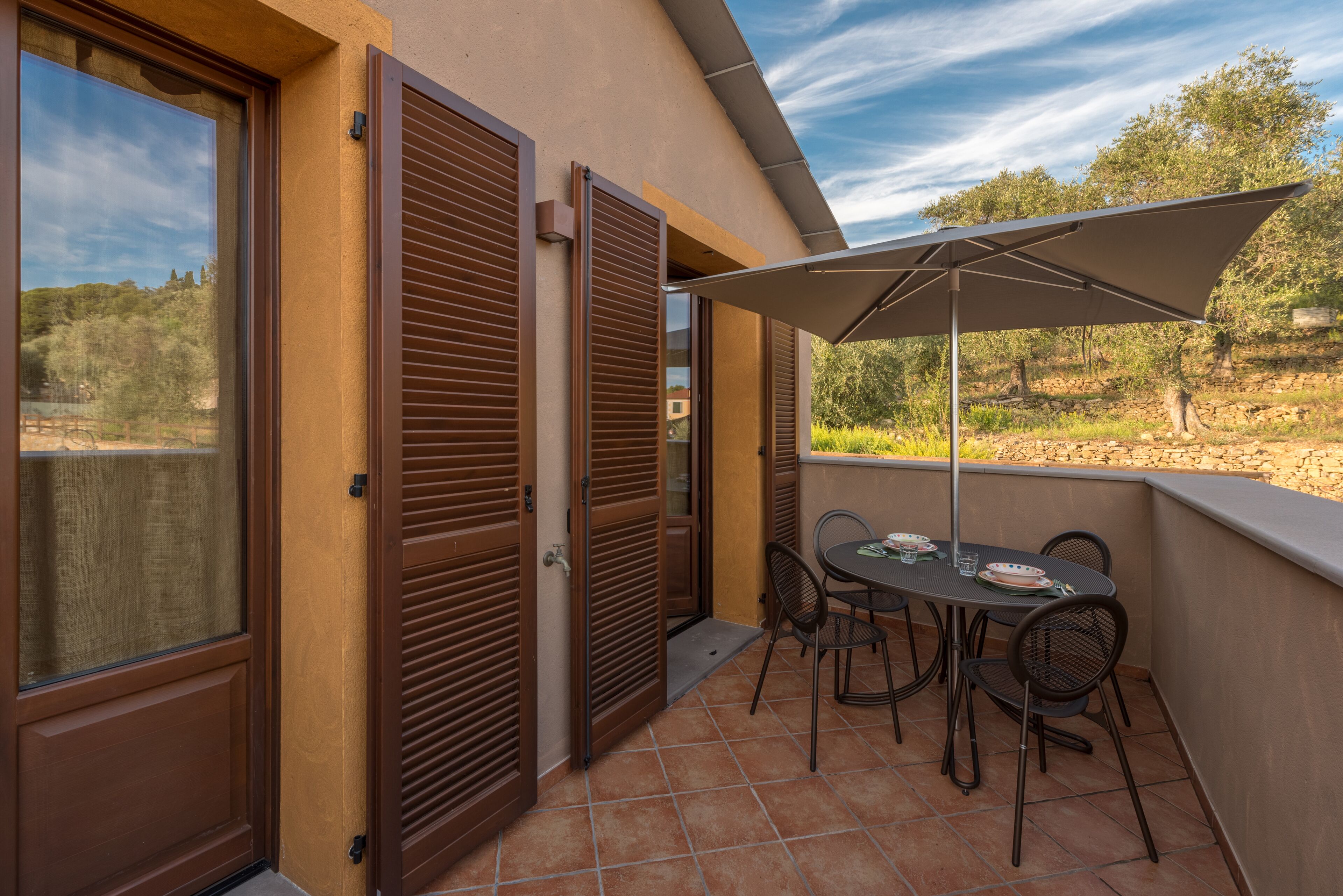 A balcony with a table and chairs, a large umbrella, and a view of the surrounding landscape.