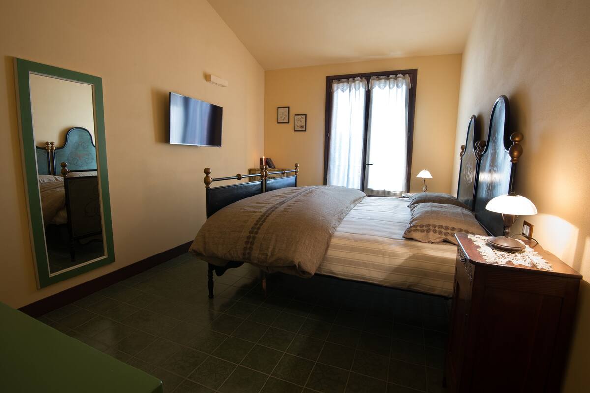 Un dormitorio con cama, cómoda, espejo, televisor y ventana con cortinas.