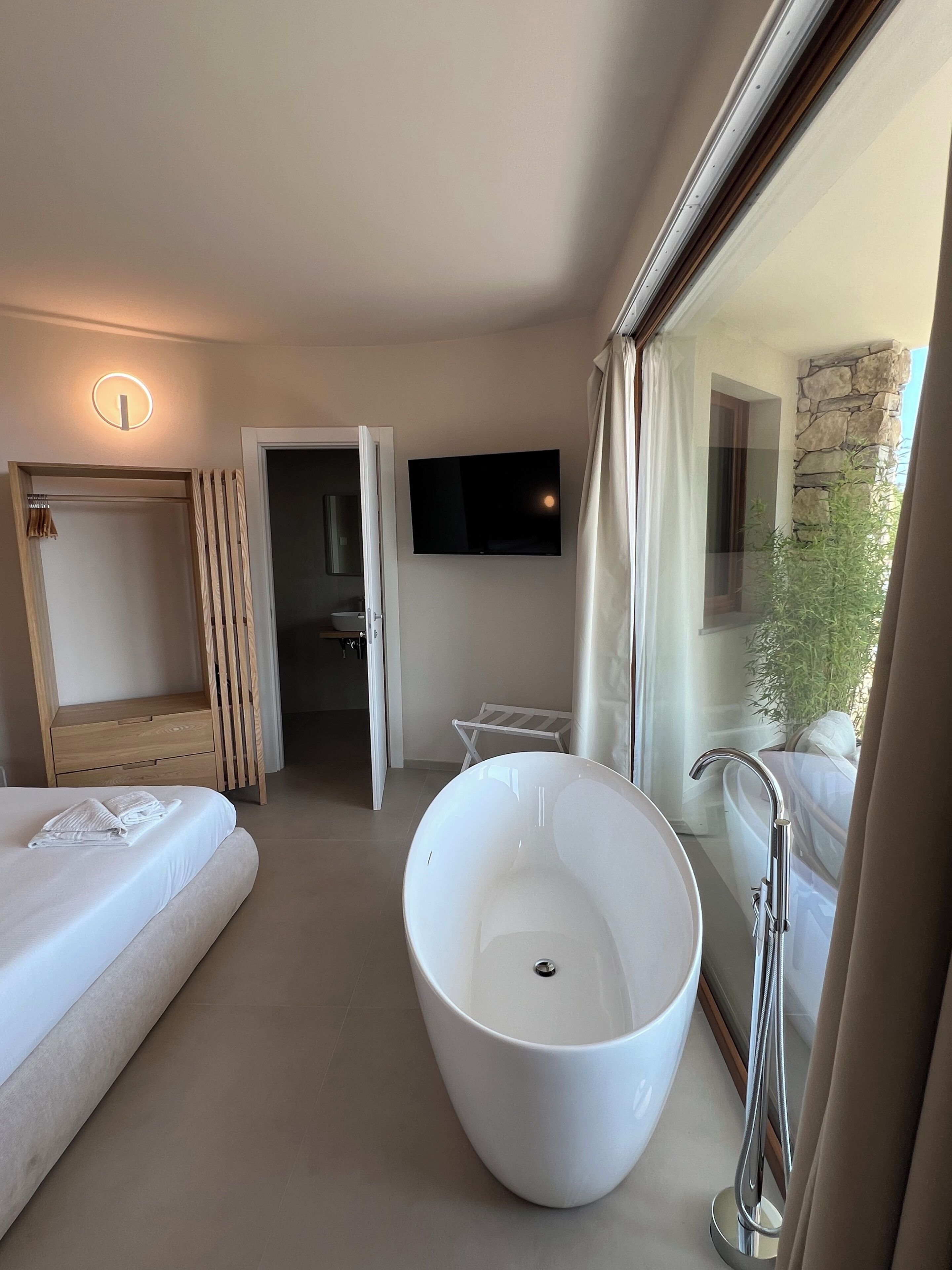 A modern bathroom with a freestanding bathtub, a large mirror, and a television mounted on the wall.