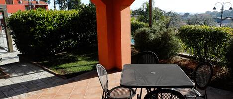 En udendørs terrasse med et bord og stole, omgivet af grønt og med udsigt over landskabet.