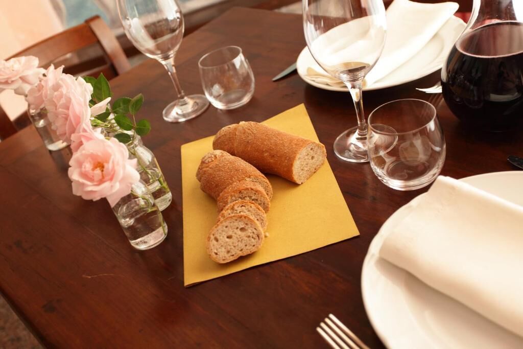 A dining table with a loaf of bread, a vase with flowers, and wine glasses.