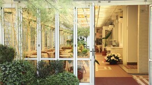 A hotel entrance with a glass door, indoor plants, and a tiled floor. - Hotel Abbazia (Grado)