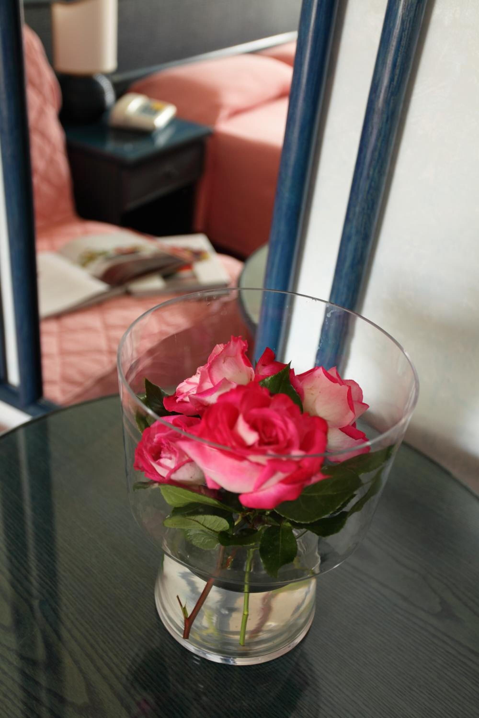 Un jarrón de vidrio transparente con rosas rosadas sobre una mesa de vidrio.