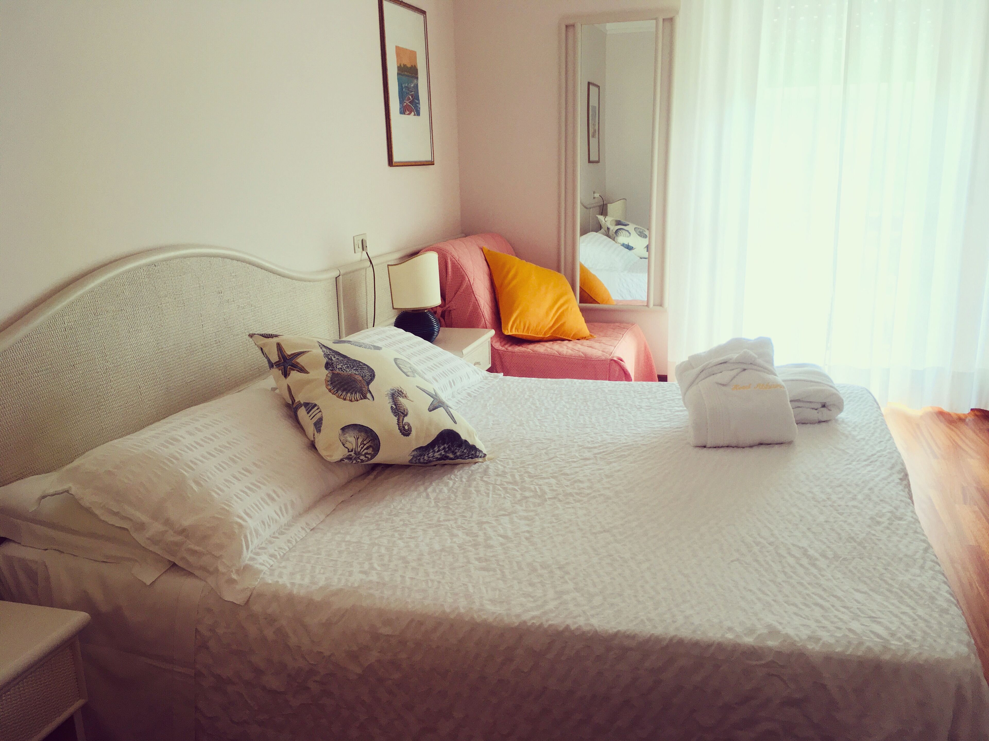 Una cama bien hecha con un cojín estampado, una lámpara de noche y una toalla doblada sobre la mesita.