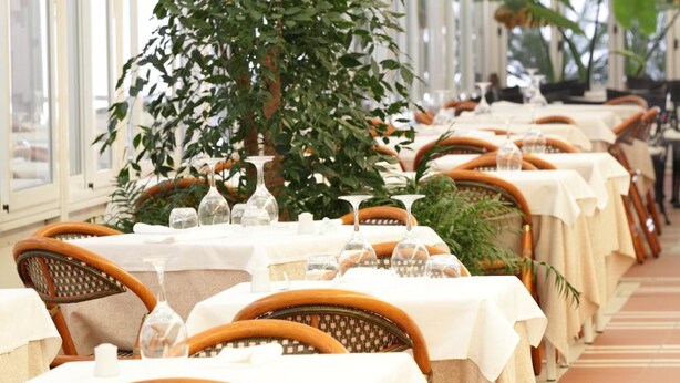 A restaurant with tables set for dining, large windows, and indoor plants. - Hotel Abbazia (Grado)