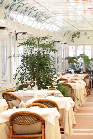 A restaurant with tables set for dining, large windows, and indoor plants. - Hotel Abbazia (Grado)