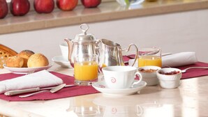 A breakfast table with a variety of fruits, a coffee pot, cups, and a vase with a white flower. - Hotel Abbazia (Grado)