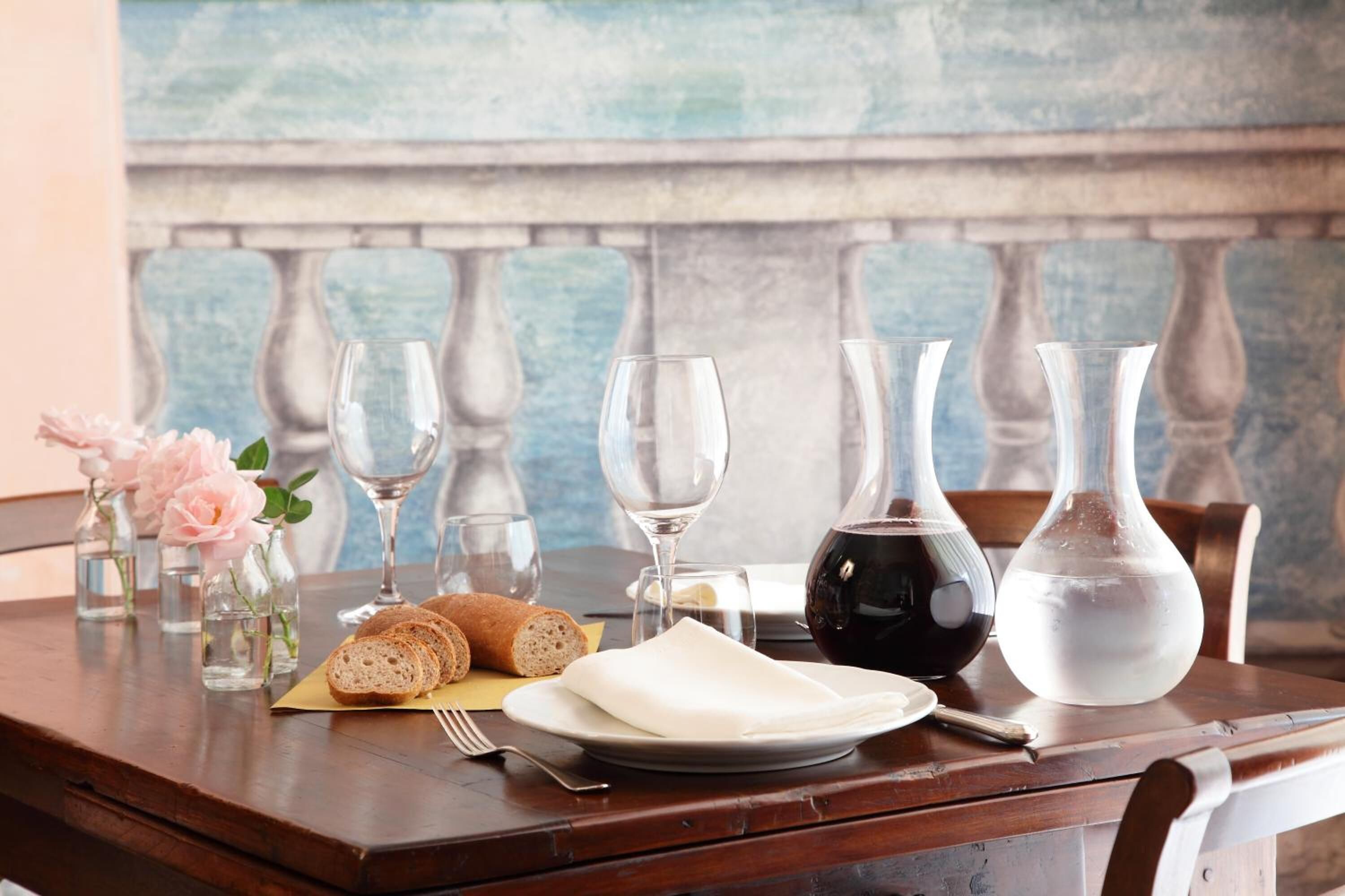 Une table en bois sur laquelle se trouvent une assiette de pain, une serviette, un verre de vin rouge et une carafe d’eau.