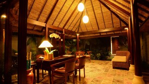 A dining area with a thatched roof, wooden furniture, and a patterned floor. - Ubud Wana Villa (Ubud)