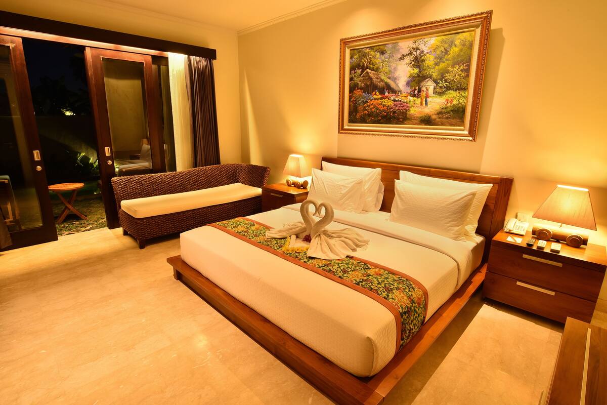 A hotel room with a large bed, a sofa, a small table, and a painting on the wall.