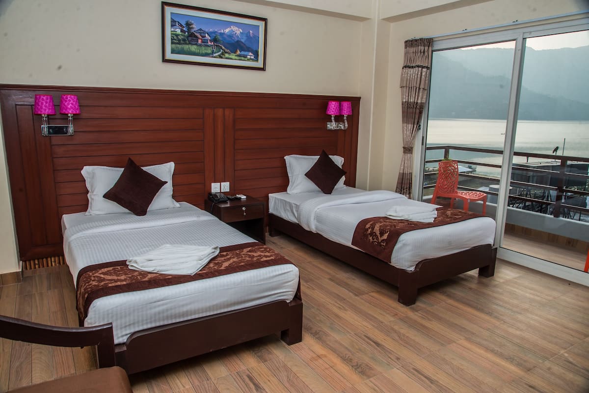 A hotel room with two beds, wooden headboards, and a large window offering a view of a lake and mountains.