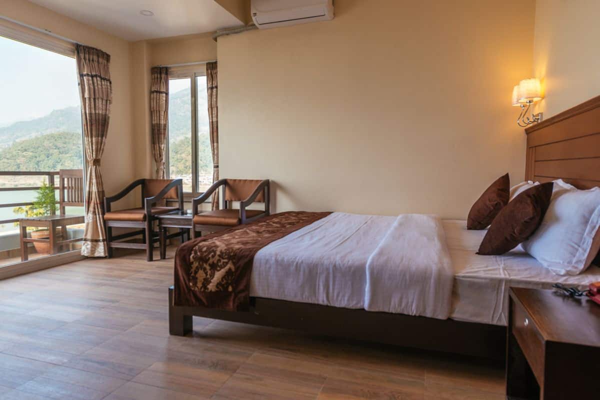 A hotel room with a bed, a desk, a chair, and a balcony with a view of the mountains.