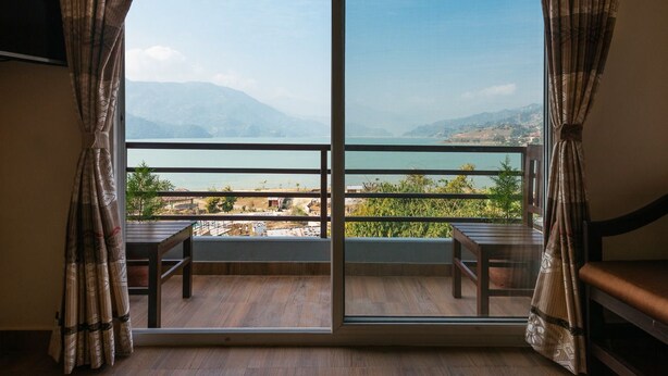A room with a large window overlooking a scenic view of mountains and a body of water. - Hotel The Coast (Pokhara)