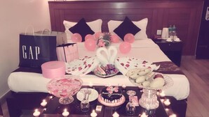 A bed with a wooden headboard, a bedside table with a cake, balloons, and a gift bag. - Hotel The Coast (Pokhara)