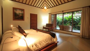 A bedroom with a bed, a chair, a door, and a large window with curtains. - Villa Sutra (Pemuteran)