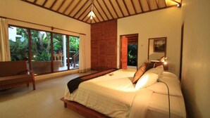 A bedroom with a large bed, a bench, and a view of greenery through the window. - Villa Sutra (Pemuteran)