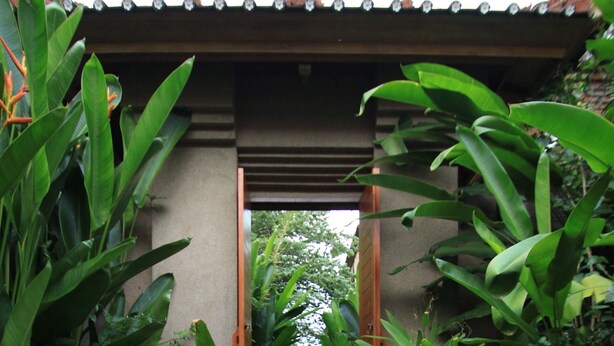 A stone pathway leading to a wooden gate, surrounded by lush greenery and a pond with lily pads. - Villa Sutra (Pemuteran)