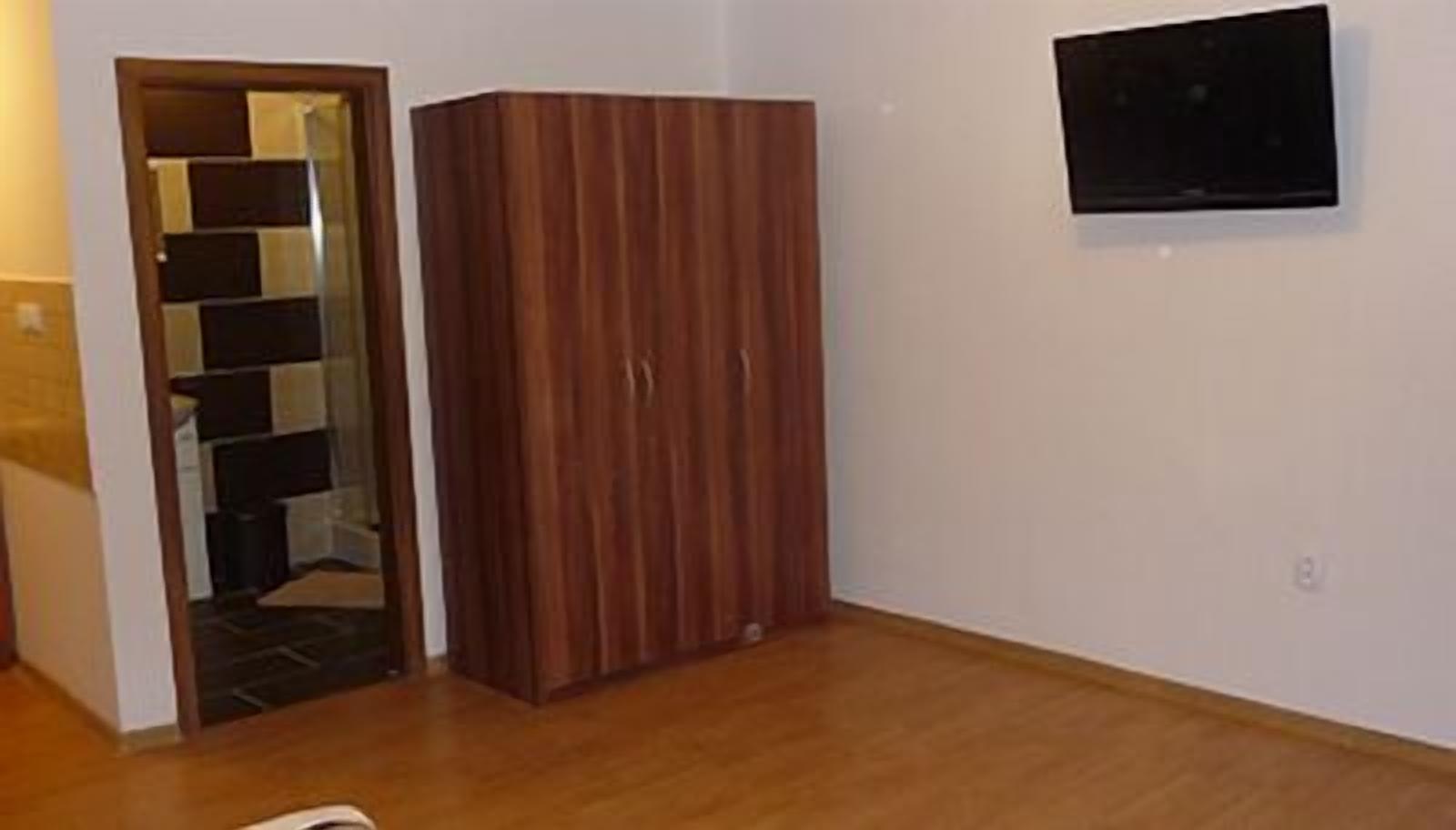 Ein Zimmer mit einem Holzschrank, einer Tür zu einem anderen Raum und einem an der Wand befestigten Fernseher.