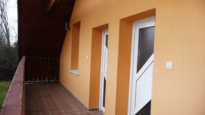 A covered outdoor area with a wooden deck, a yellow wall, and two white-framed doors. - Apartmány STAR (Bobrovec)