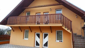 A two-story building with a balcony, a wooden staircase, and a brick wall. - Apartmány STAR (Bobrovec)