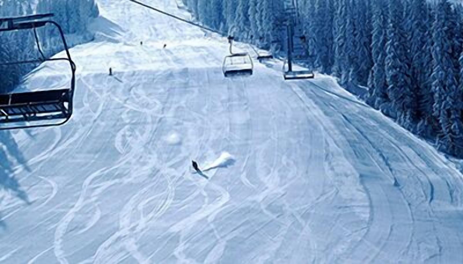 A ski lift chair moving along a snowy slope with tracks and trees in the background.