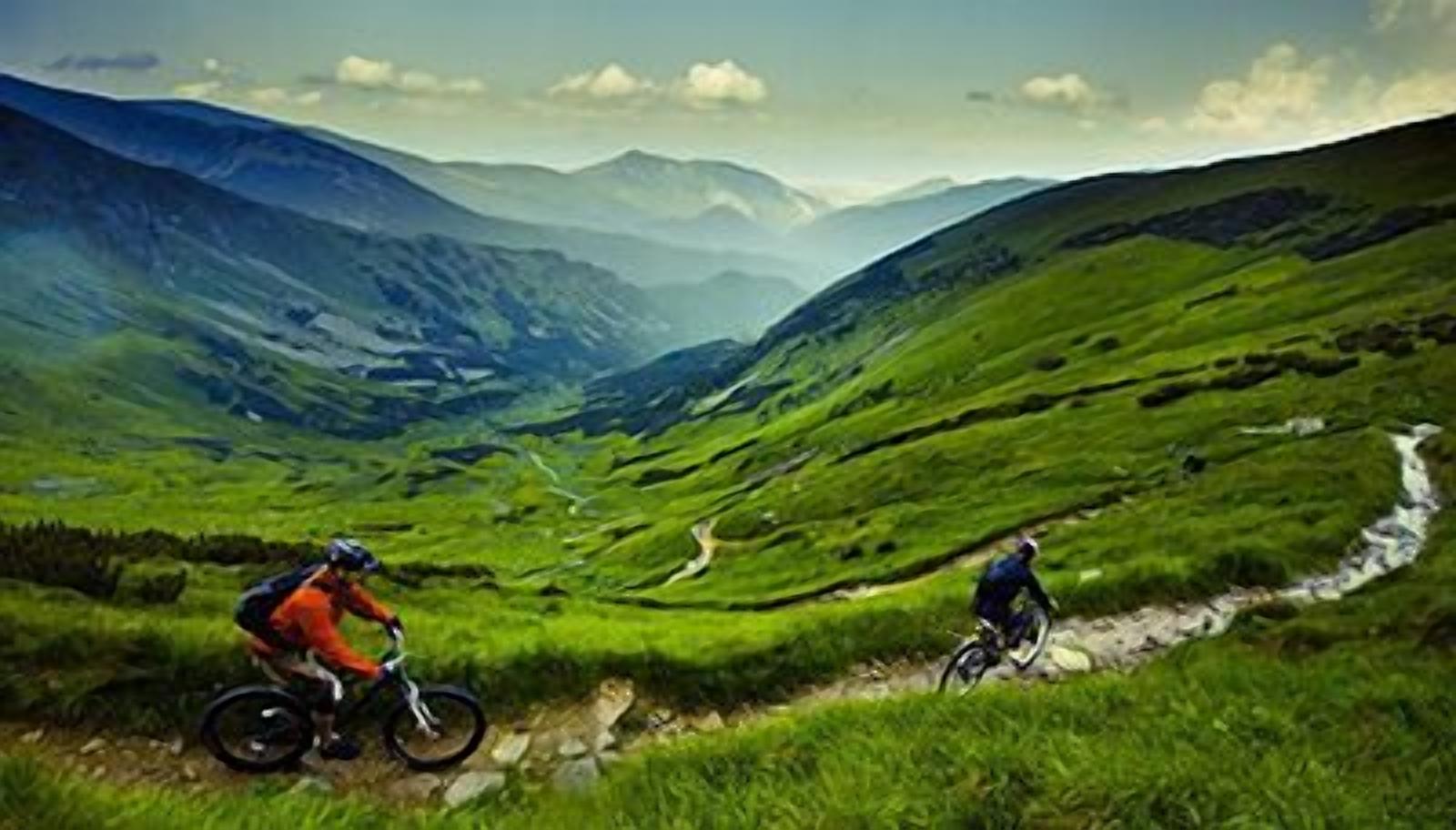 A mountain biking trail with lush green hills and a river.