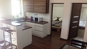 A compact kitchen with a microwave, sink, and bar stools. - Apartmány STAR (Bobrovec)