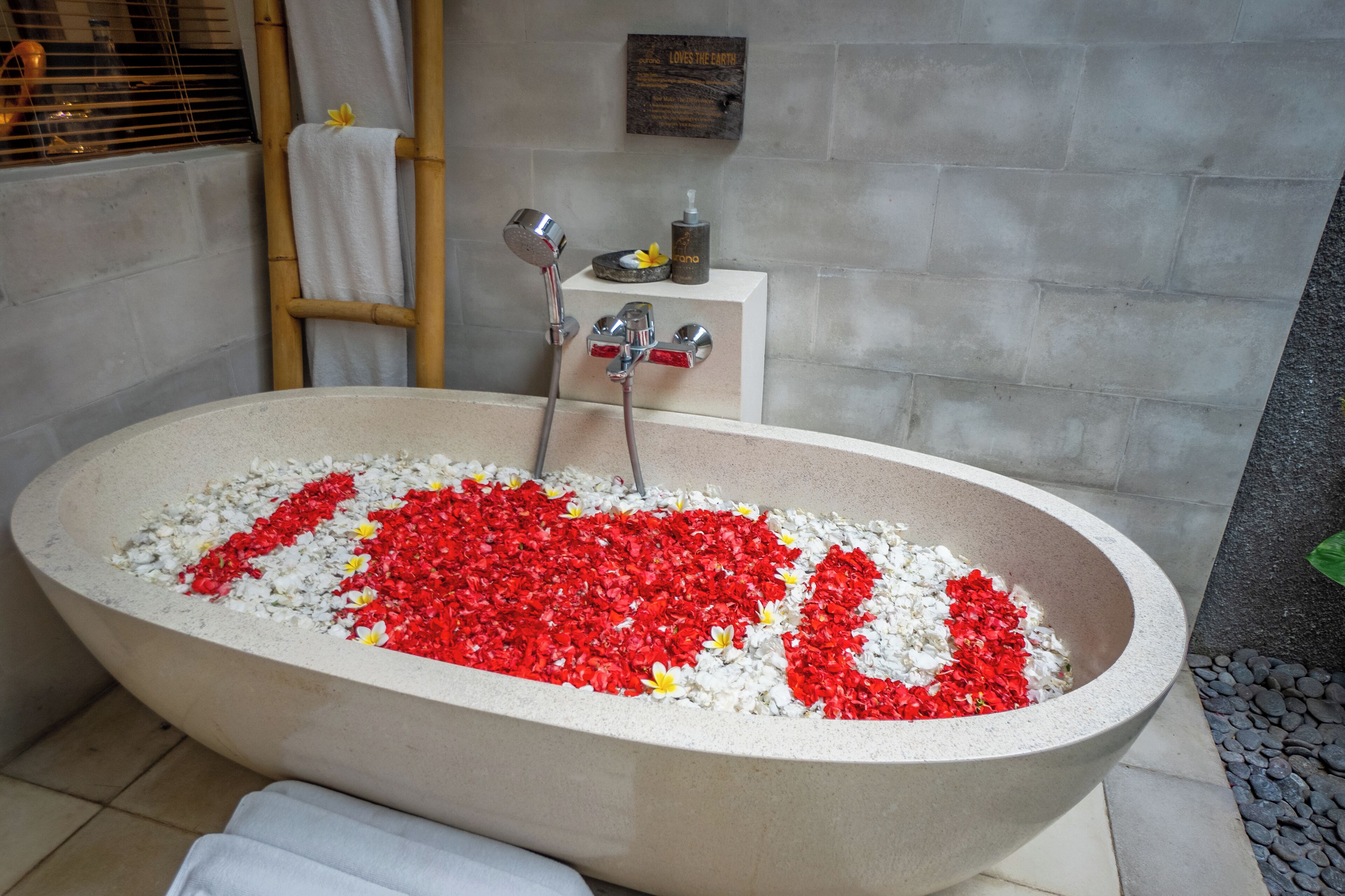 Una bañera llena de agua y pétalos de flores rojos y blancos dispuestos en forma de corazón.