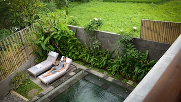 A pool area with two lounge chairs and a small table, surrounded by lush greenery and a bamboo fence.