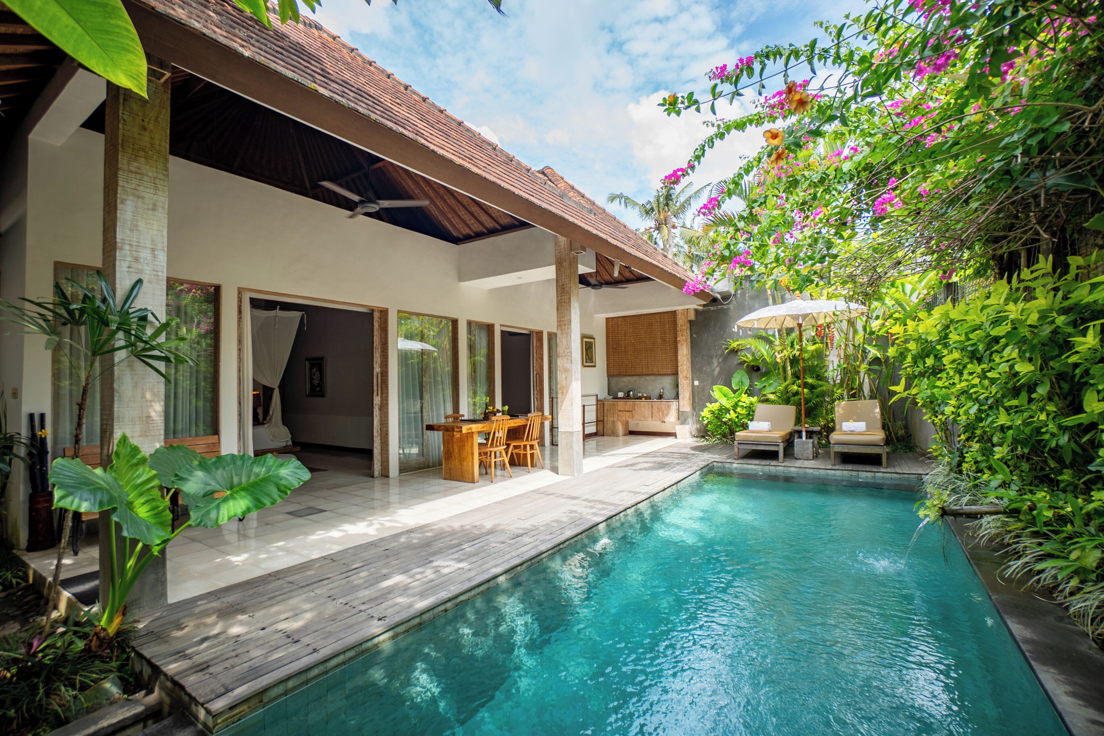 A poolside area with a wooden deck, a dining table with chairs, and a covered seating area with lounge chairs.