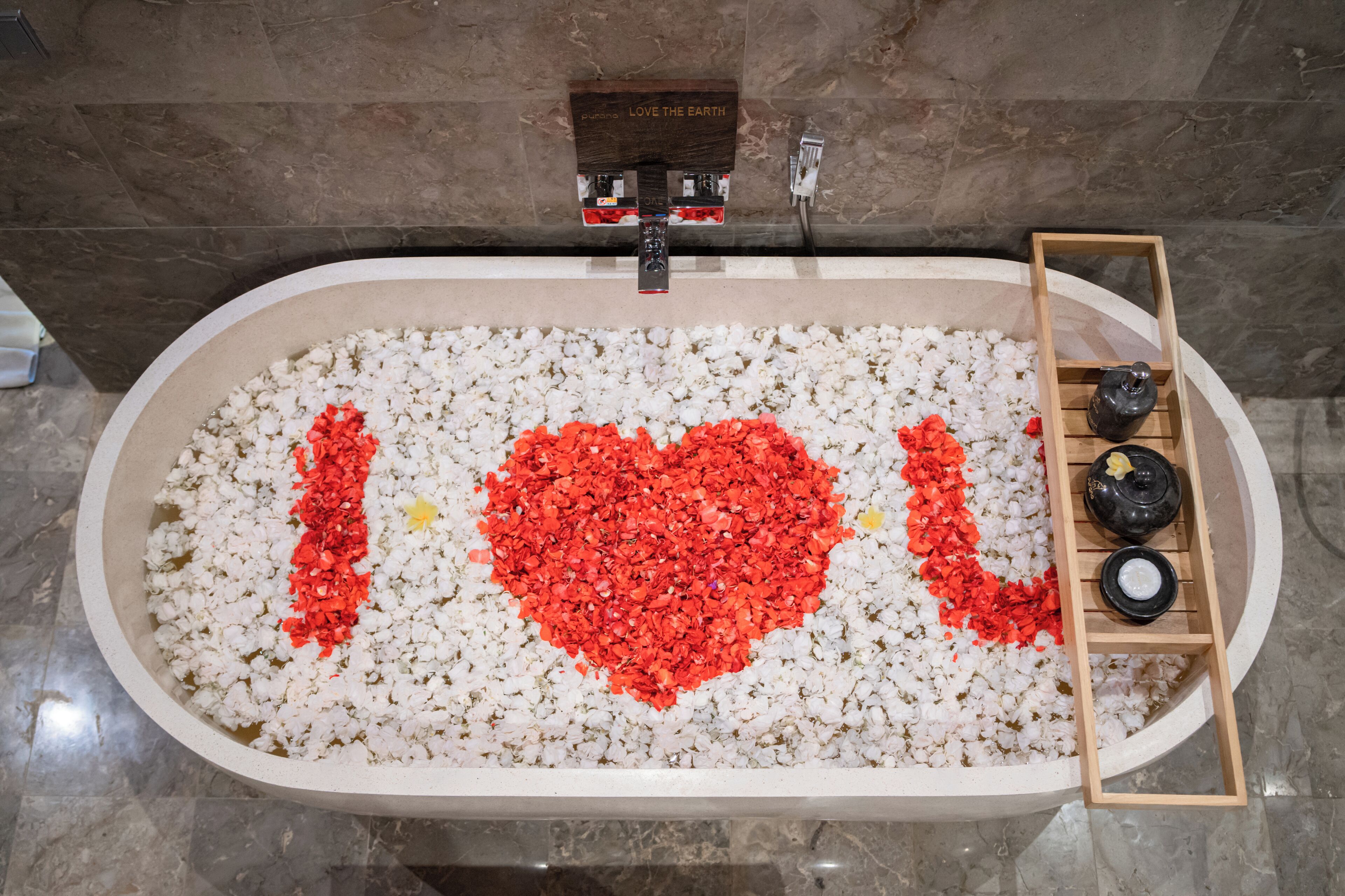 A bathtub filled with white pebbles and red heart-shaped decorations spelling "I ♥ L."