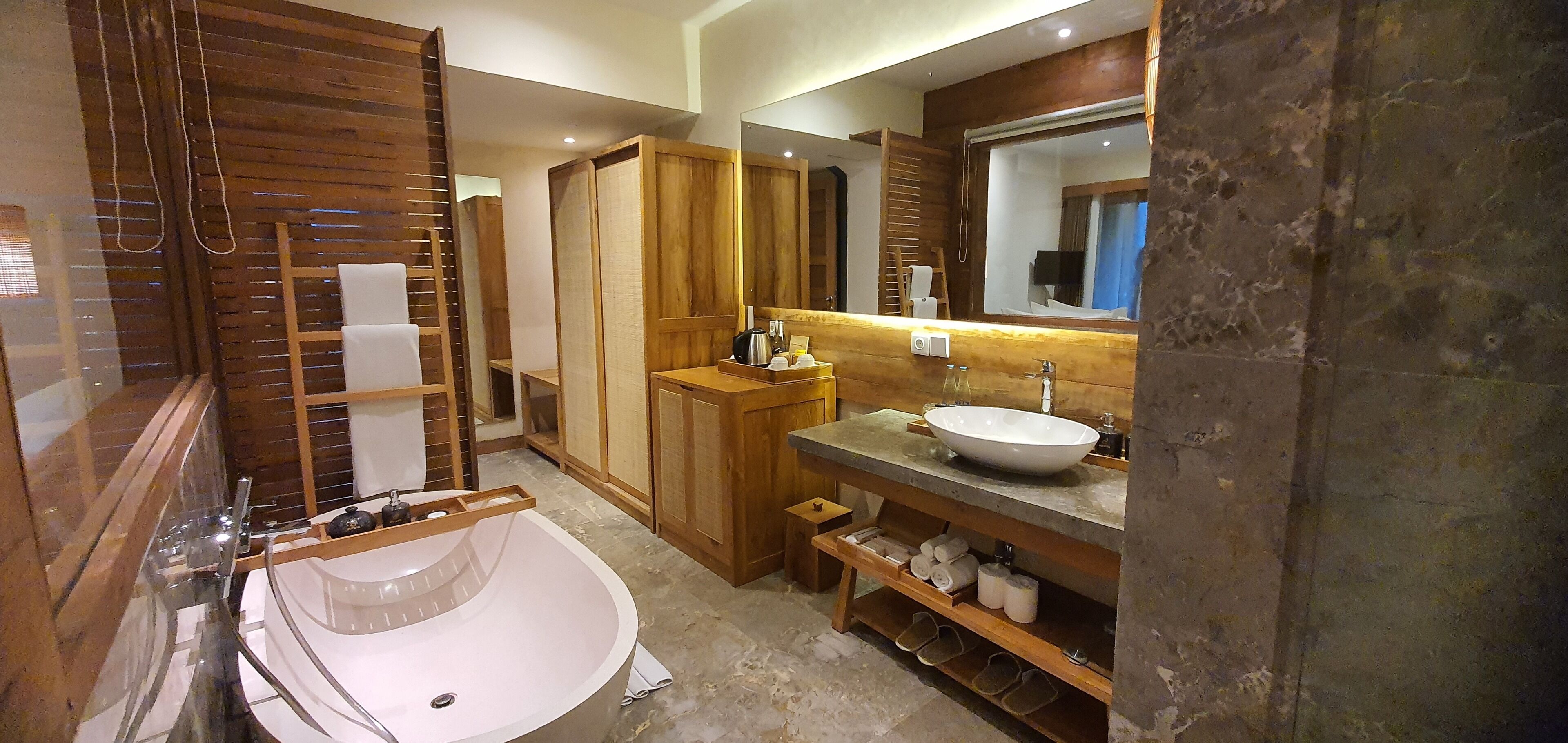 A bathroom with a freestanding bathtub, wooden cabinets, a large mirror, and a vanity with a sink.