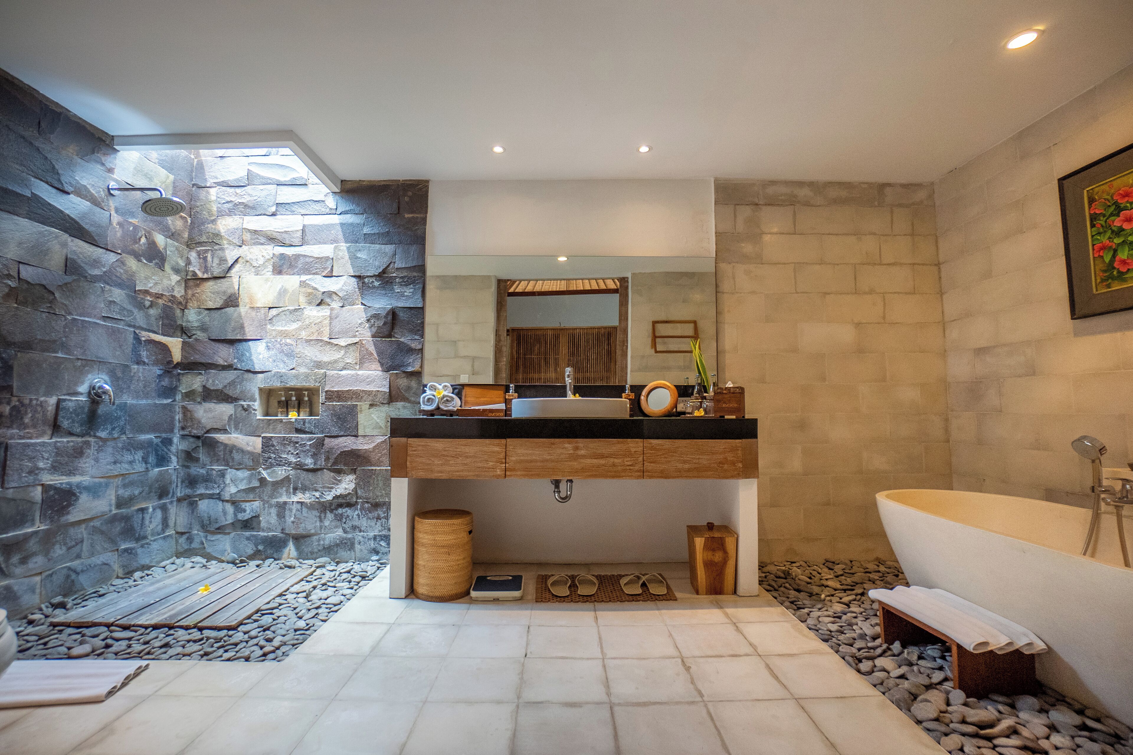 A modern bathroom with a stone accent wall, a large bathtub, and a vanity with a mirror.