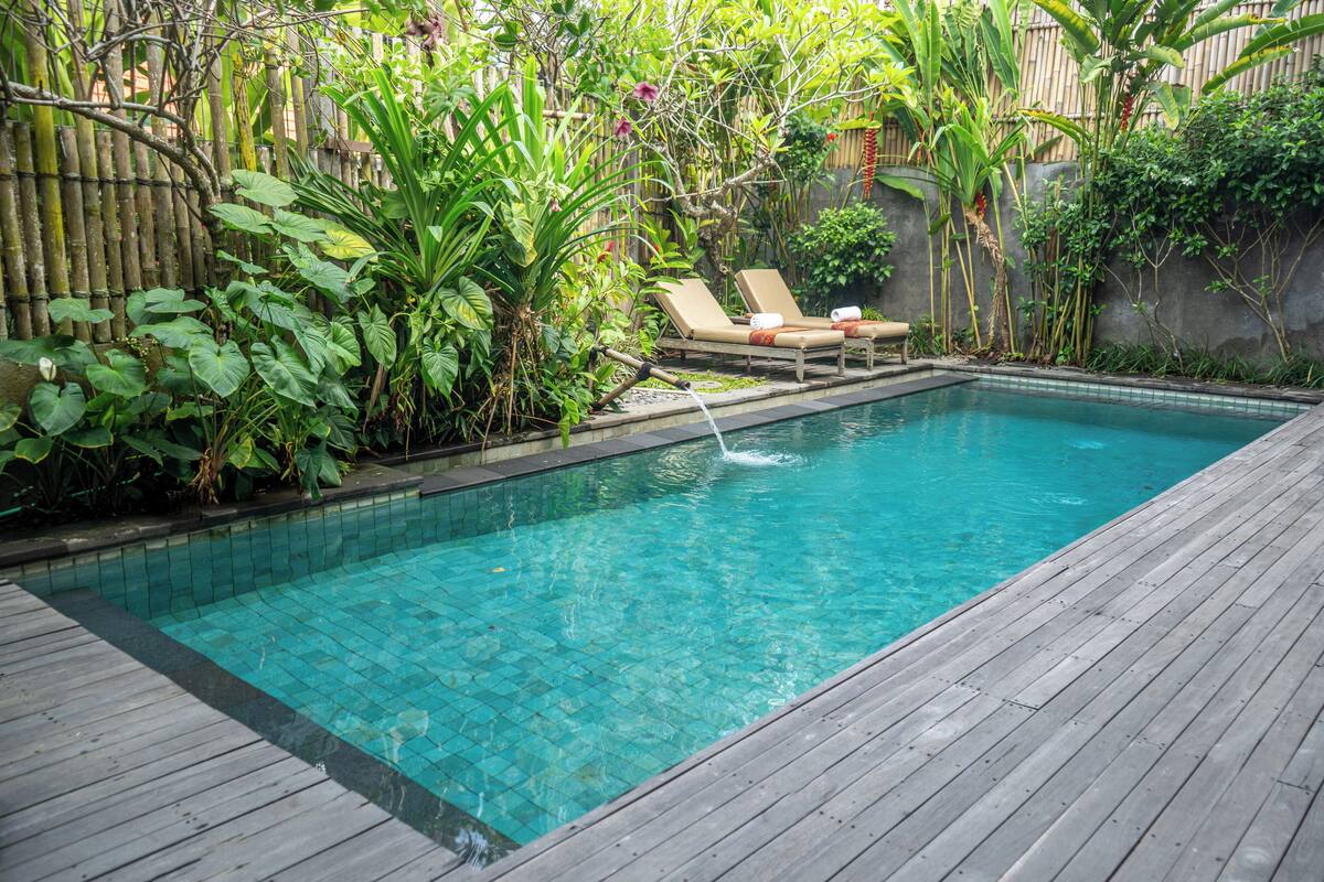A rectangular swimming pool with clear blue water, surrounded by lush greenery and a wooden deck.
