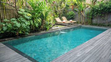 A rectangular swimming pool with clear blue water, surrounded by lush greenery and a wooden deck.