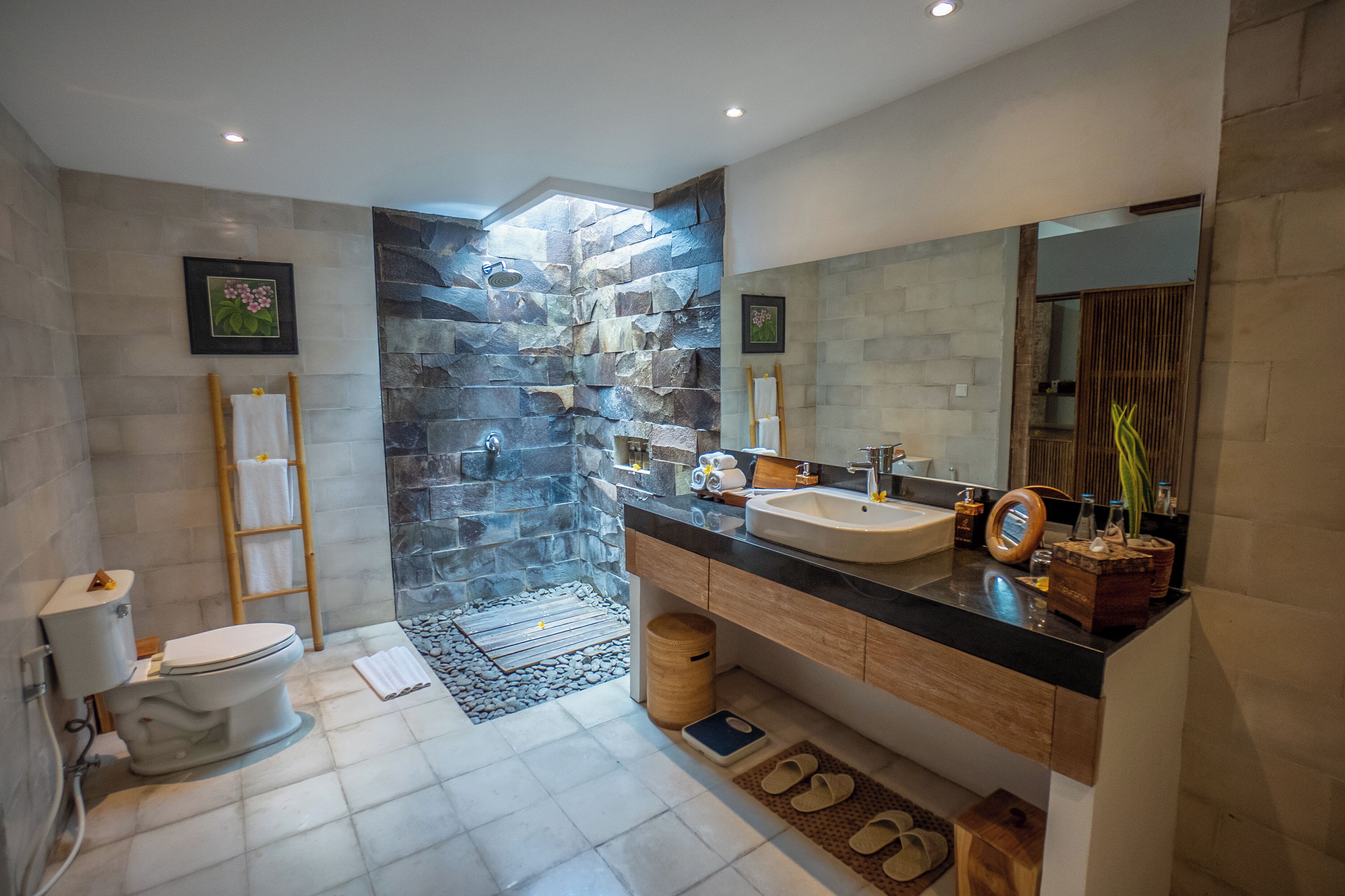 A modern bathroom with a stone accent wall, a large mirror, and a wooden vanity.