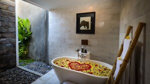 Un baño con una bañera llena de pétalos de flores, un cuadro en la pared y una escalera de bambú.