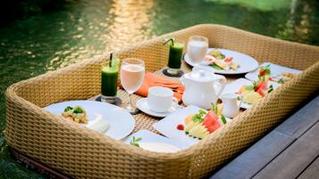 Een rieten dienblad met een picknickopstelling aan het water, inclusief borden met eten, drinken en een theepot.